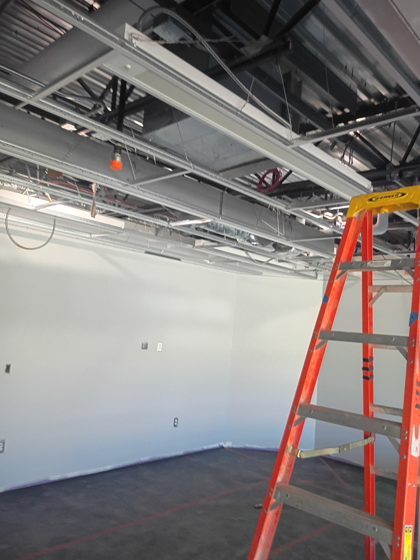 Open ceiling grid with conduits, junction boxes, and recessed light fixtures being installed