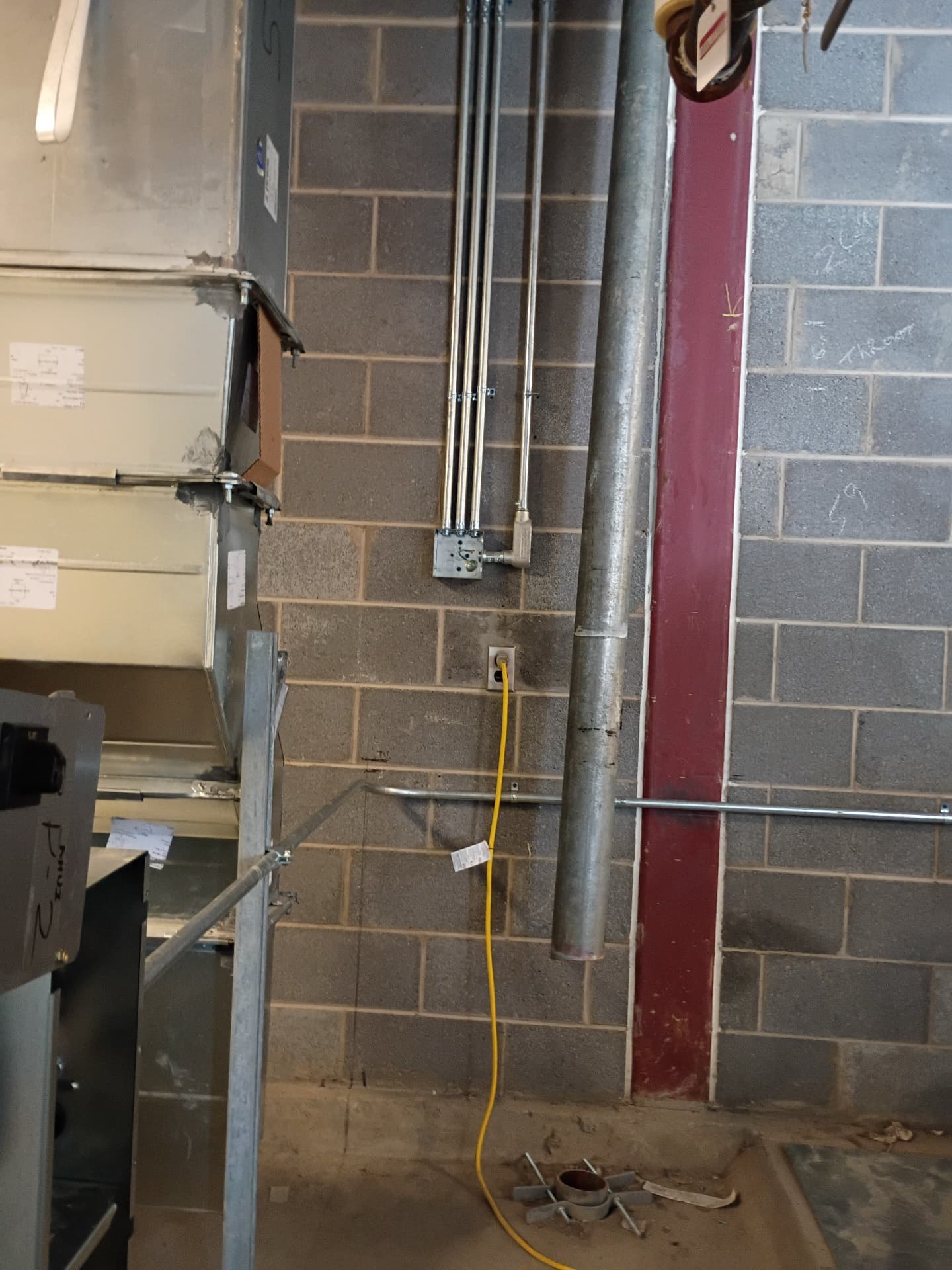 Multiple conduit runs mounted to a cinder-block wall next to HVAC ductwork